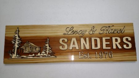 Redwood sign with cabin and evergreen trees surrounding cabin with husband and wife name and marriage date